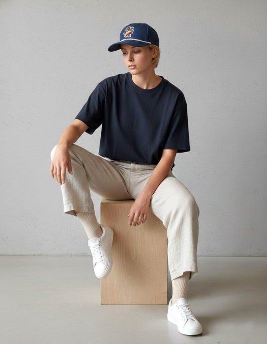 Man in a black t-shirt and white sneakers seated, wearing the navy RallyFuel rope hat