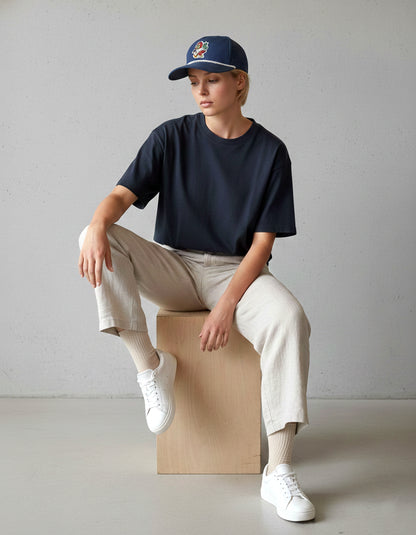 Man in a black t-shirt and white sneakers seated, wearing the navy RallyFuel rope hat